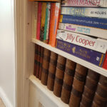 Close up of faux book spines, the one sticking out has a finger pull on the underside.